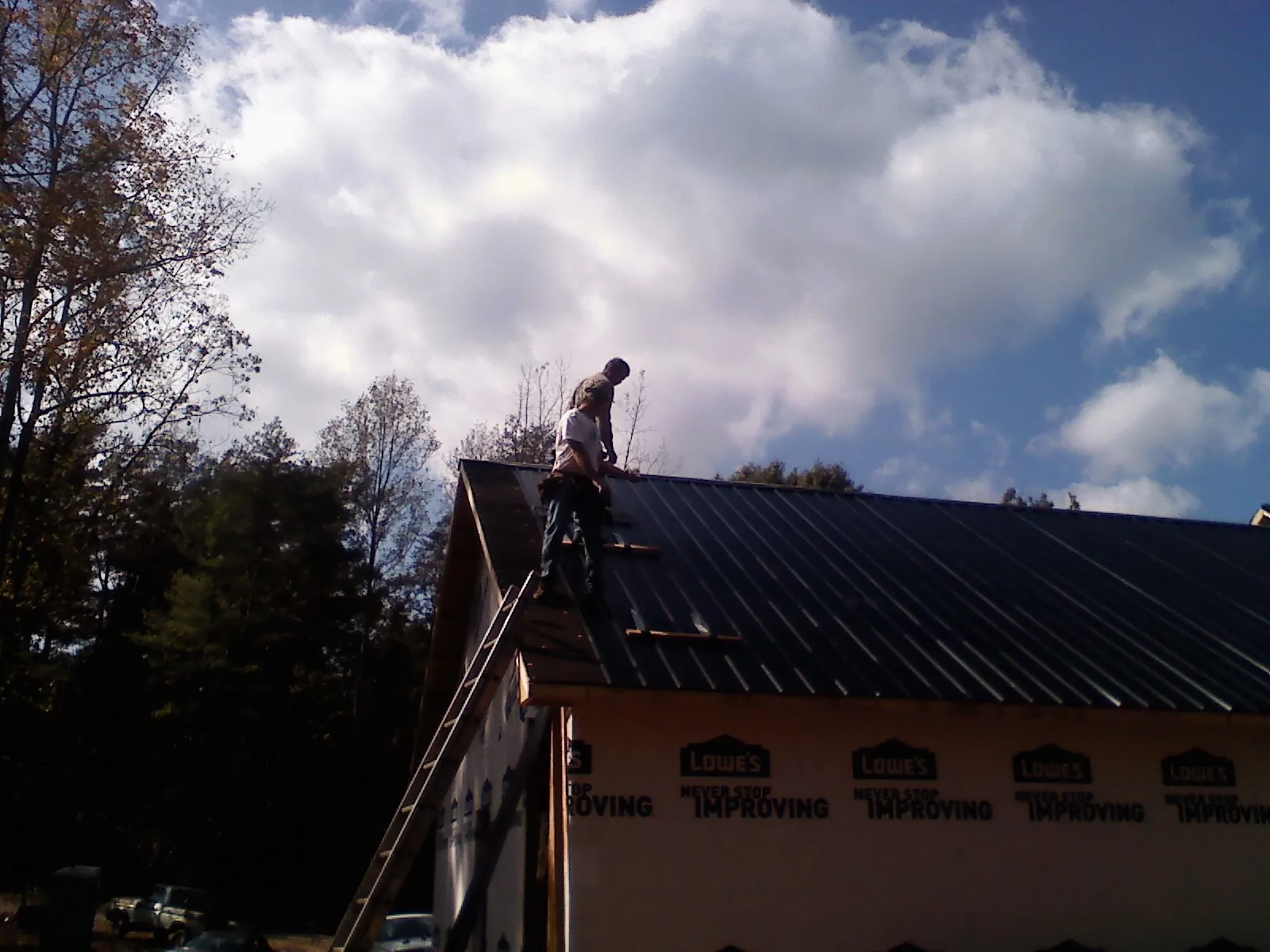 Roofer fastening dark metal panels high against a cloudy sky, from a Roof Inspection job in Cle Elum