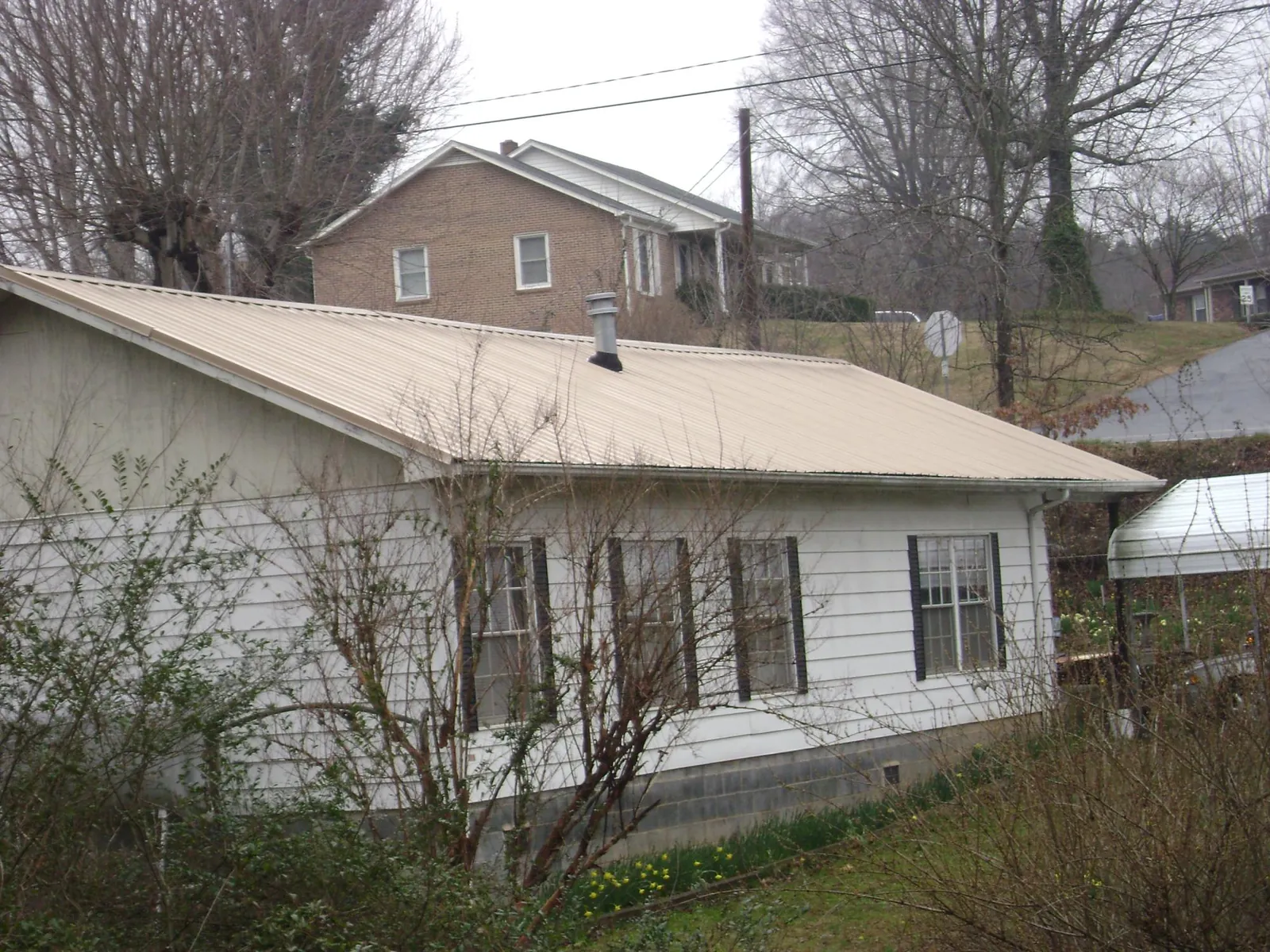 Tan metal roof on a white sided house set into a hillside — Commercial Roofing by Roofing Brothers in Cle Elum